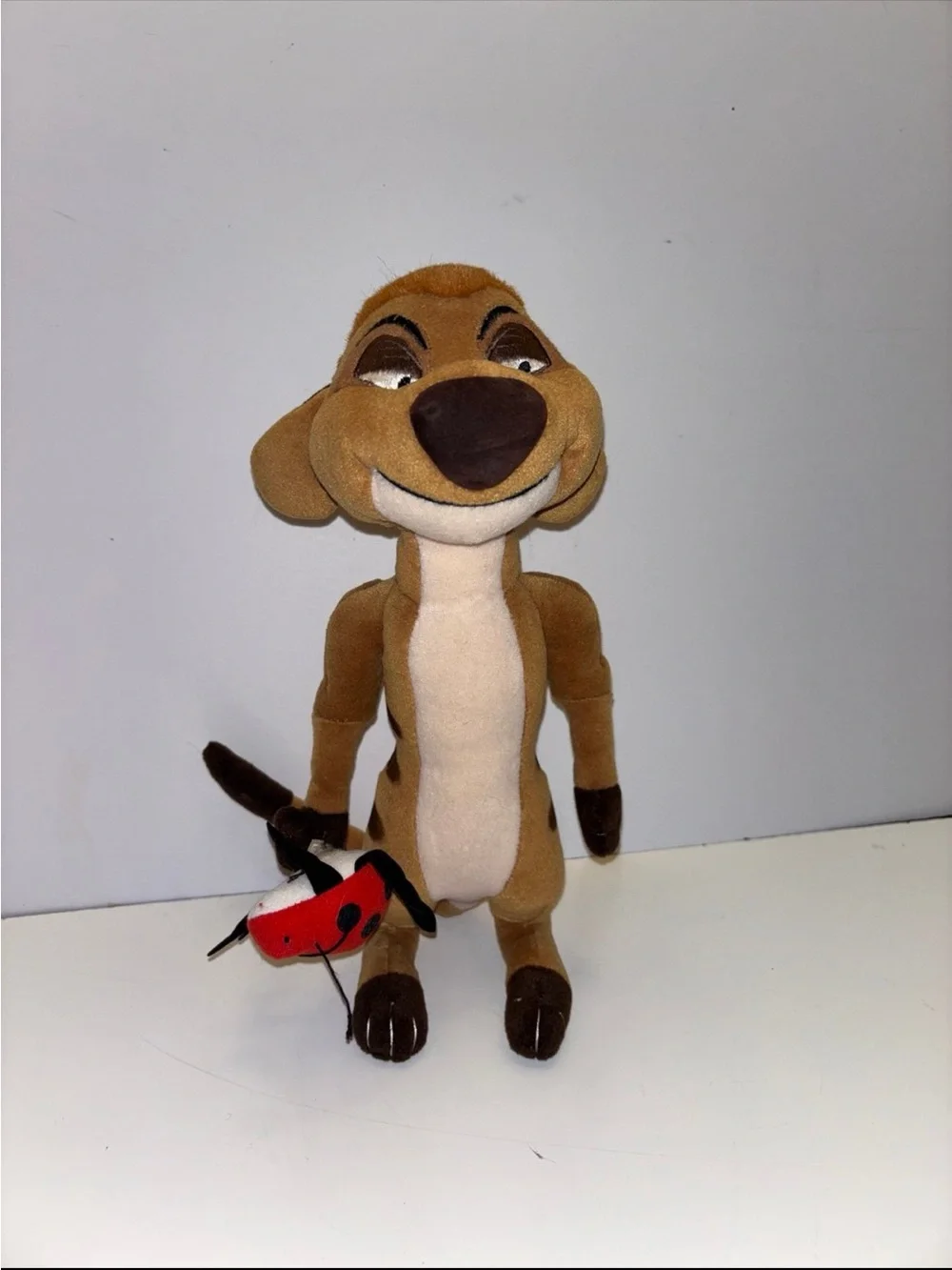 Disney The Lion King Timon plush toy holding a small red ladybug